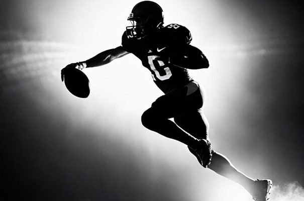 Black and white silhouette of a football player running with the ball.