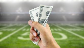 A Hand Holding Money over a Football Field as a Background