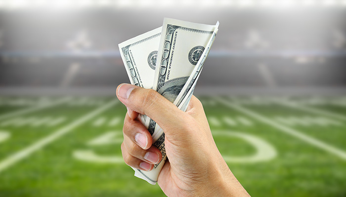 A Hand Holding Money over a Football Field as a Background